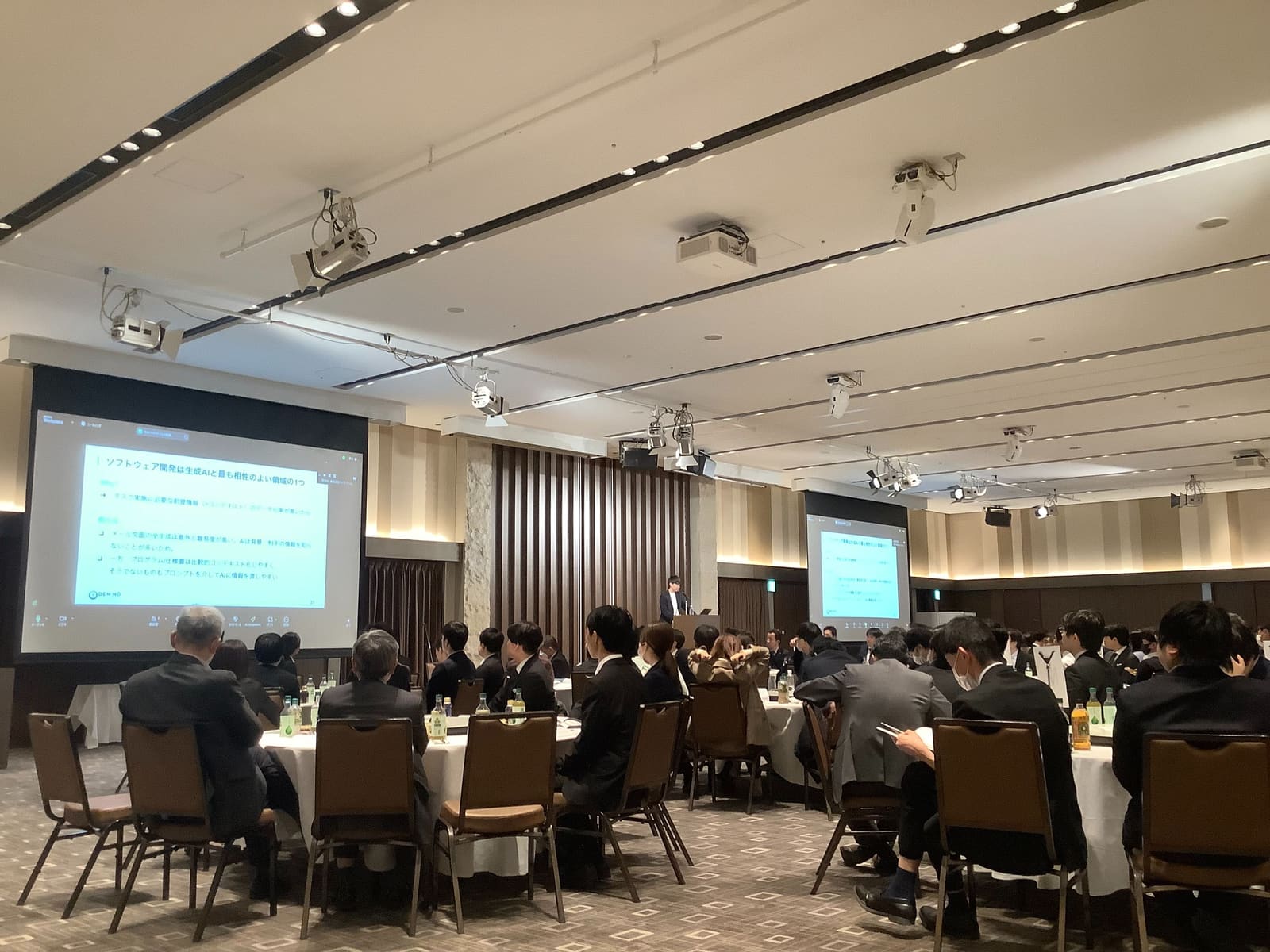 ウイズ・ワン様新年会の会場で、スクリーンを前に基調講演を行う様子